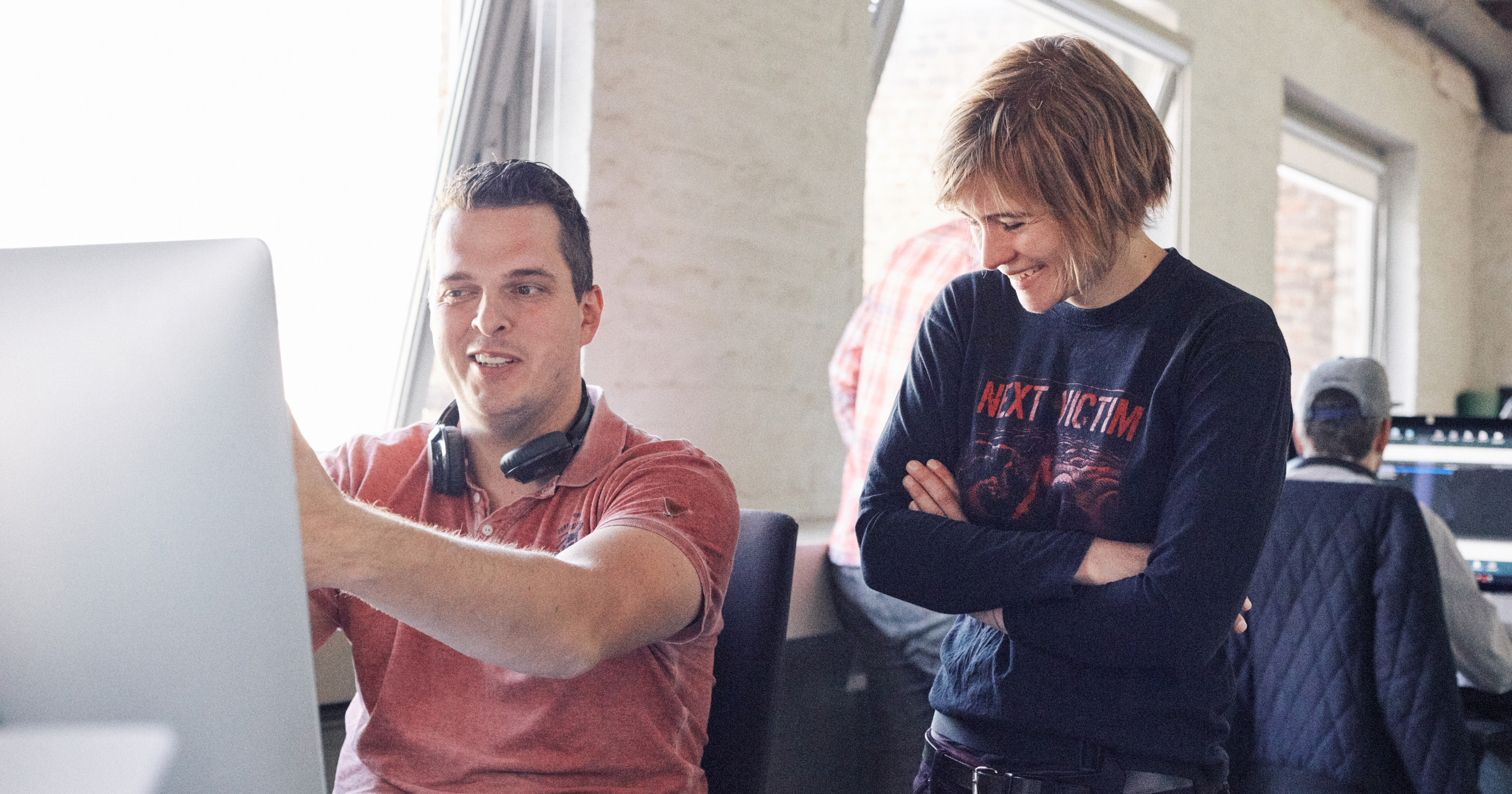 Man sieht zwei Mitarbeiter von FederhenSchneider, eine Frau und einen Mann, vor einem Monitor, die lachen.