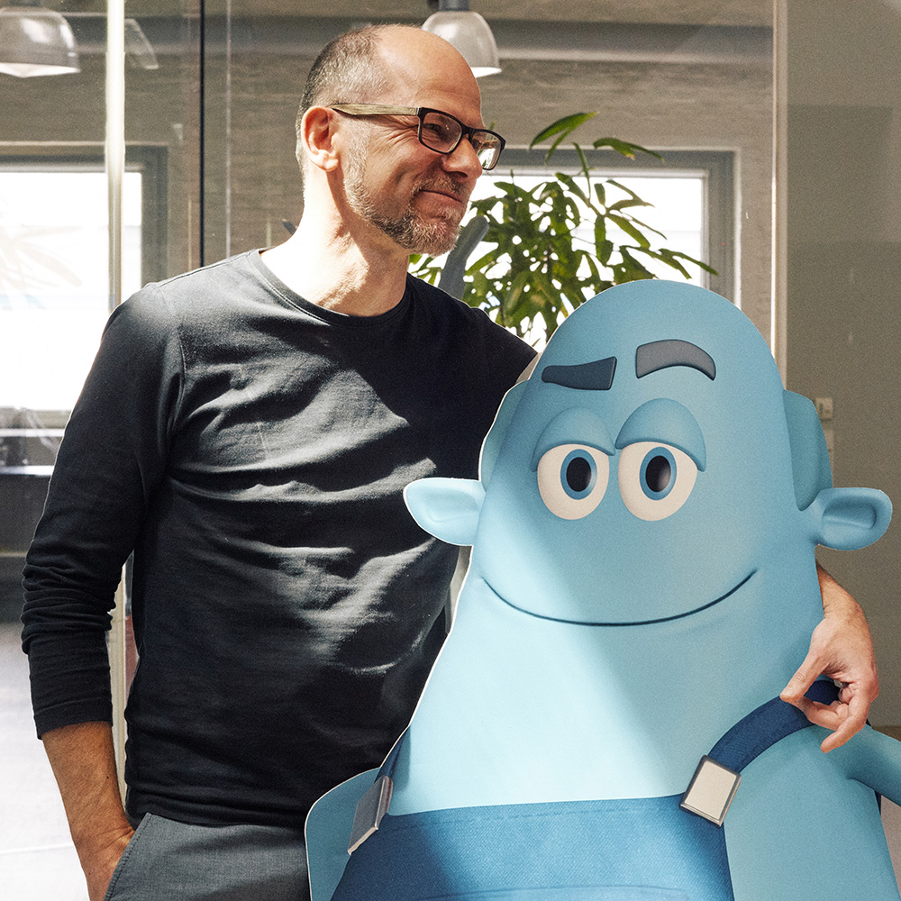 Man sieht einen FederhenSchneider Mitarbeiter, der eine blaue Pappfigur mit Blaumann umarmt.