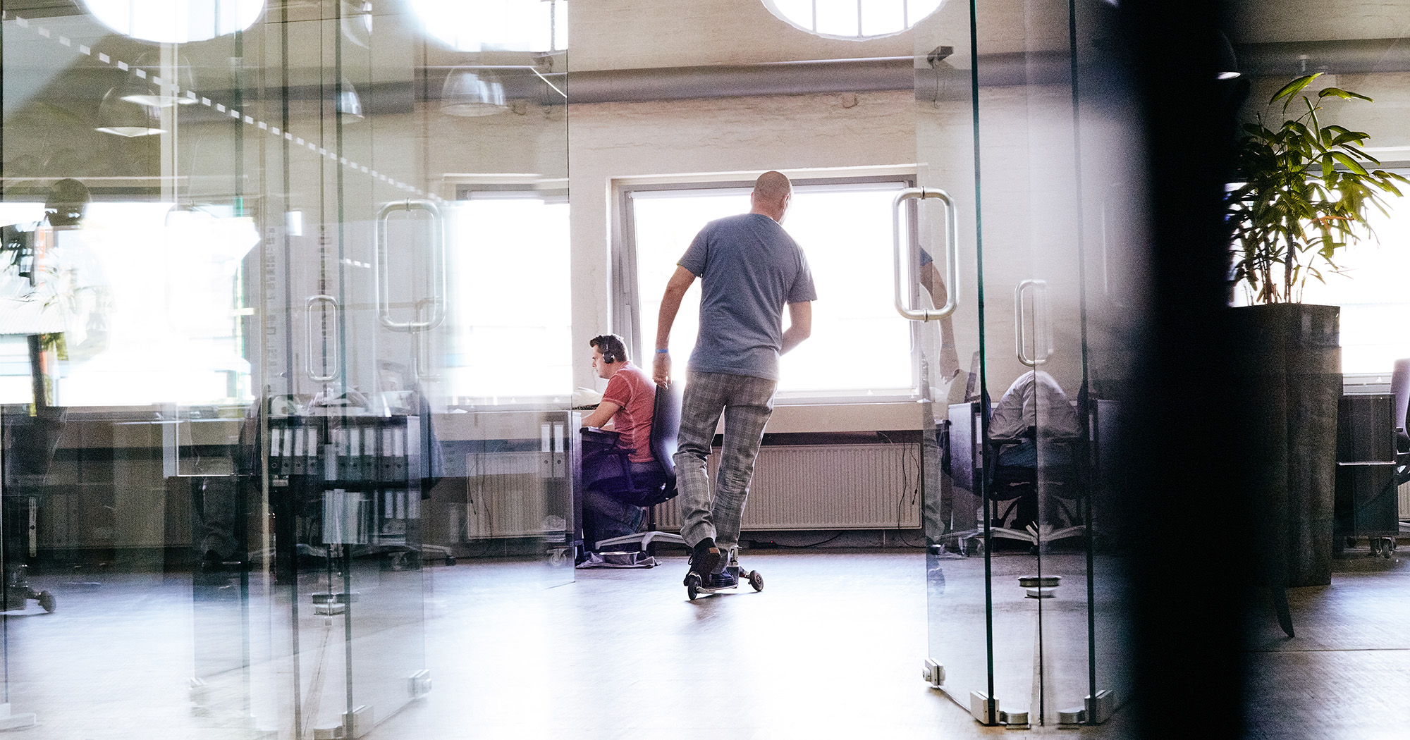 Das Bild zeigt einen der FederhenSchneider Geschäftsführer von hinten, wie er auf einem Cityroller durch den Gang der Agentur fährt.